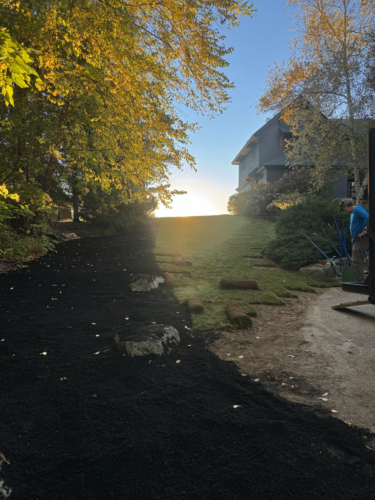 Fresh mulch bed and new sod being installed beside a home at sunset